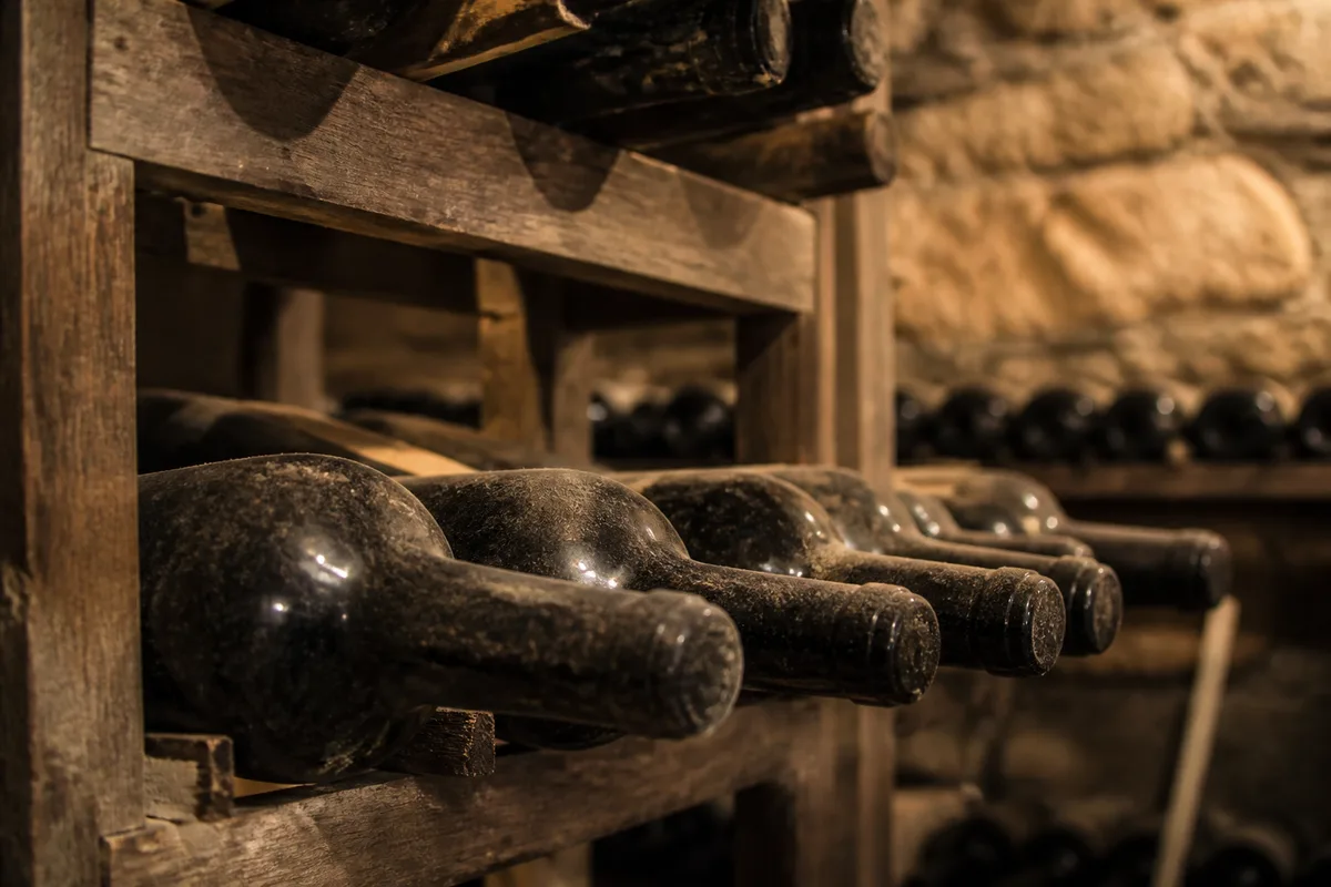 Bouteilles couchées dans des casiers de bois d&rsquo;une cave voûtée faiblement éclairée