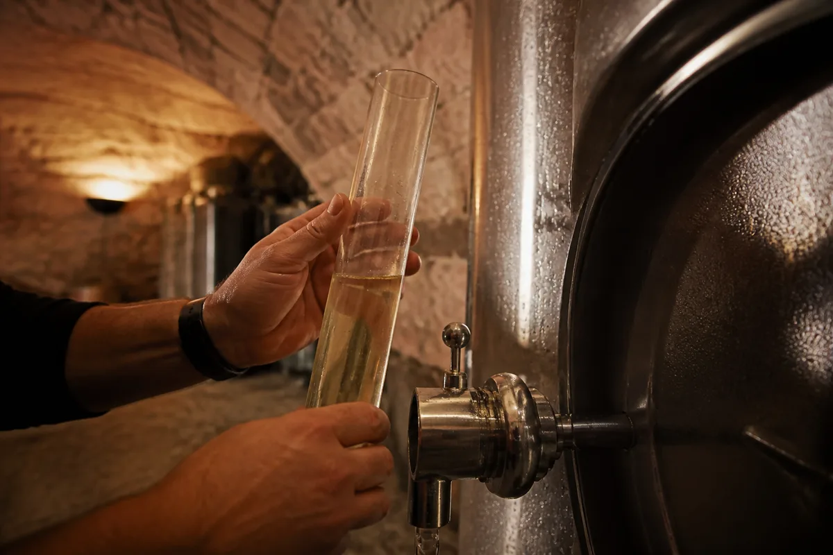 Mains d&rsquo;un vigneron relevant un niveau de cuve dans une cave voûtée