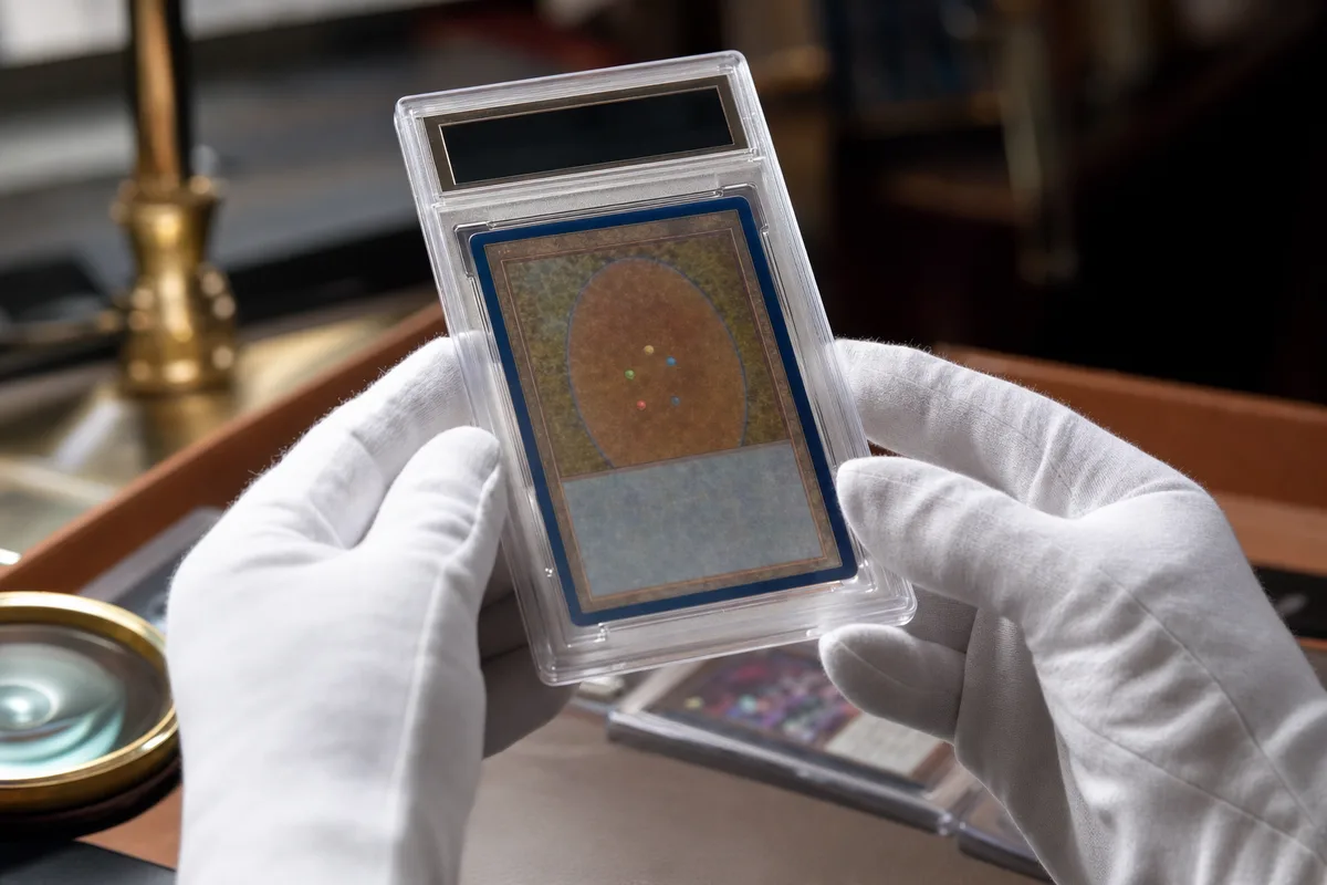 Carte à collectionner sous coque de protection rigide tenue au-dessus d’un bureau éclairé